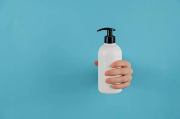 A womans hand sticks out of a hole in a blue paper background and holds a skin lotion pump. — Stock Photo, Image