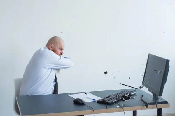 Un calvo enojado con barba roja en la oficina con traje de negocios choca contra una computadora. Manager con una crisis nerviosa rompe el teclado en la pantalla . —  Fotos de Stock