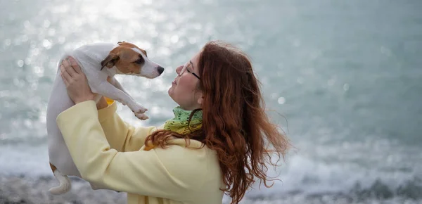 Biała rudowłosa kobieta trzymająca na wybrzeżu psa Jacka Russella Terriera. — Zdjęcie stockowe