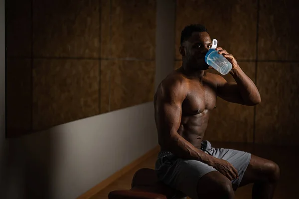 Afroameričan bez košile pije z koktejlu v tělocvičně. — Stock fotografie