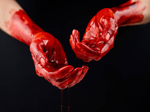 Womens hands in blood on a black background.