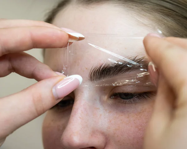 El maestro utiliza una película de plástico durante la laminación de las cejas. — Foto de Stock