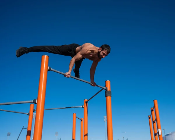 Egy férfi meztelen felsőtesttel egyensúlyt teremt a vízszintes korláton.. — Stock Fotó