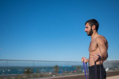 Tişörtsüz adam dışarıda lastik bantlarla egzersiz yapıyor.. 