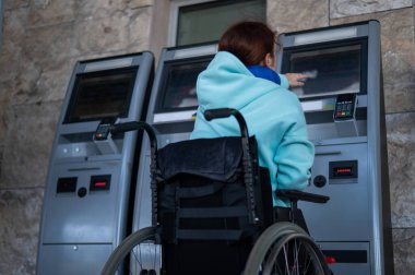 Tekerlekli sandalyedeki beyaz bir kadın tren istasyonundaki self servis kasasına ulaşamaz. Ulaşılması zor bir ortam.