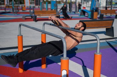 Spor sahasındaki paralel çubuklarda üstsüz adam yatay denge yapıyor.. 