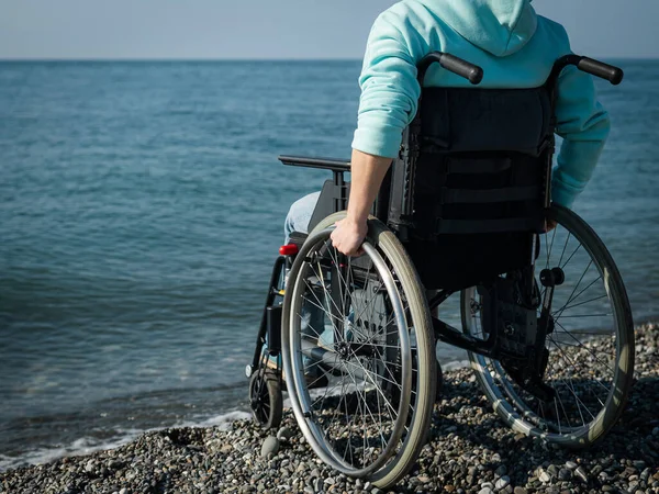 Donna caucasica su una sedia a rotelle sulla riva del mare. Primo piano delle mani femminili. — Foto Stock
