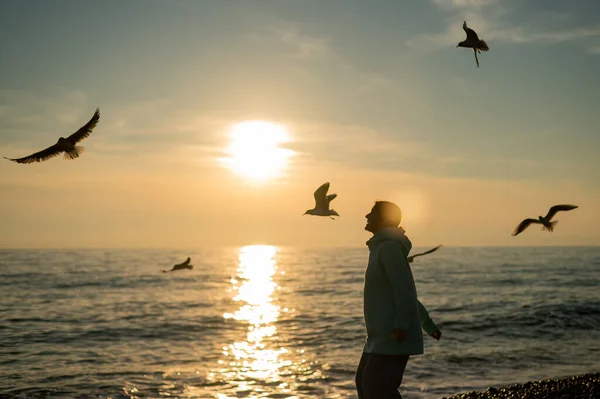 Femme blanche nourrissant les mouettes au coucher du soleil au bord de la mer. — Photo