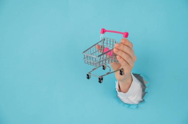 Avucunda alışveriş arabası olan bir kadın eli kağıt mavisi arka planda bir delikten dışarı sarkan.. 