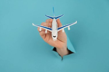 Mavi arka planda bir delikten dışarı sarkan bir kadın el bir uçak modeli tutar.. 