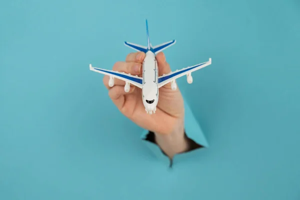 A female hand sticking out of a hole from a blue background holds a model of an airplane.