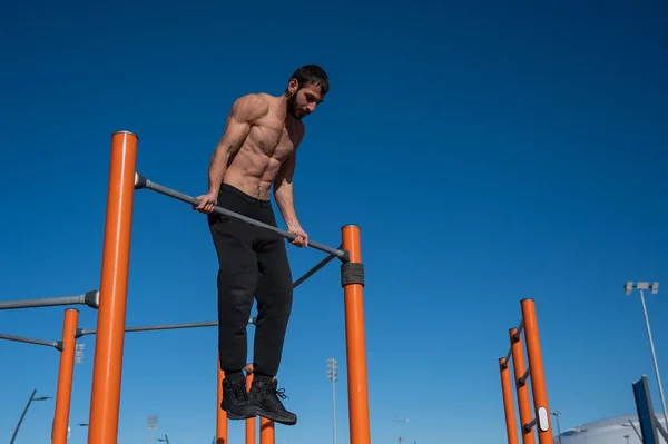 Hombre sin camisa tirando hacia arriba en la barra horizontal al aire libre. — Foto de Stock