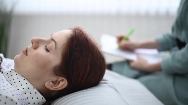 一位高加索女人躺在沙发上表达自己的感受，而一位心理学家则在平板电脑上做笔记. — 图库视频影像