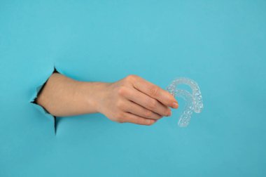 Mavi arka planda bir delikten dışarı sarkan bir kadın eli, çıkarılabilir gece koruyucularını tutar.. 