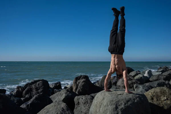 Uomo a torso nudo che fa stand su rocce in riva al mare. — Foto Stock