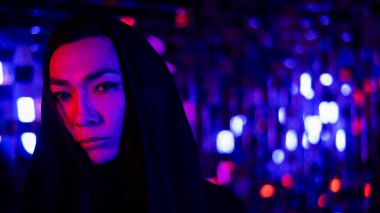 Kapüşonlu bir androjenik modelin yakın plan portresi. Stüdyoda neon ışıklı bir erkek transseksüel..