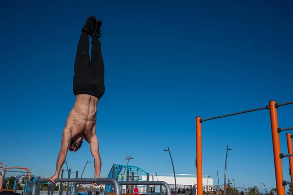 Shirless άνθρωπος κάνει handstand σε παράλληλα μπαρ στο γήπεδο του αθλητισμού. — Φωτογραφία Αρχείου