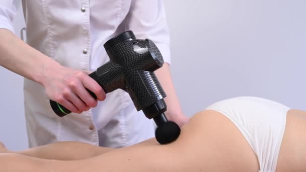 El médico masajea el muslo del paciente con un masajeador eléctrico con una pistola. — Vídeo de stock