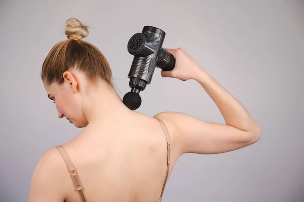Vit kvinna ger sig själv en ryggmassage med pistol. — Stockfoto
