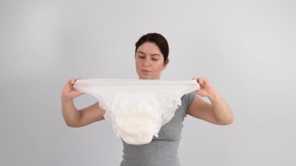 A caucasian woman holds an adult diaper and checks its strength on a white background. — Stock Video