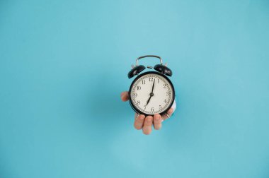 Bir kadın mavi kağıttan bir arka planda bir delikten dışarı çıkar ve çalar saati tutar. Boşluğu kopyala. 