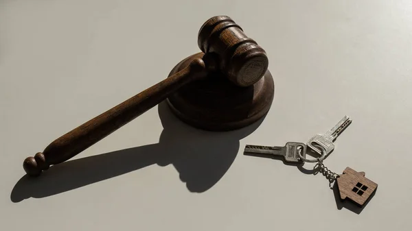 Keys with a keychain in the shape of a house and a judges gavel on a white background. — Stock Photo, Image