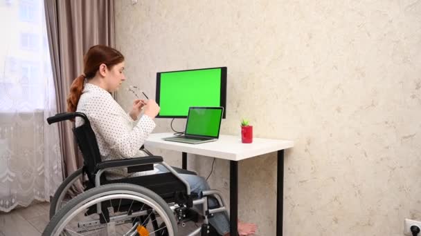 Caucasian woman with disabilities working at the computer while sitting in a wheelchair. — Wideo stockowe