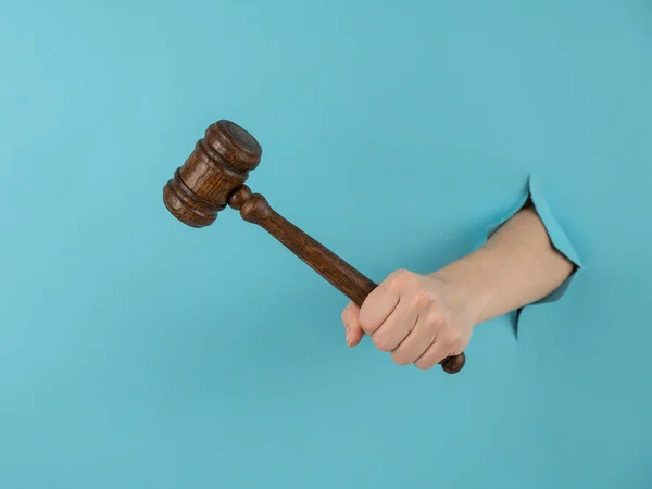 A womans hand with a wooden judges gavel sticks out of a hole in a blue background. — Stock Photo, Image