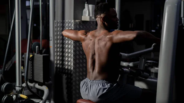 Shirtless afro-americano fazendo exercícios de volta em uma máquina no ginásio. — Fotografia de Stock