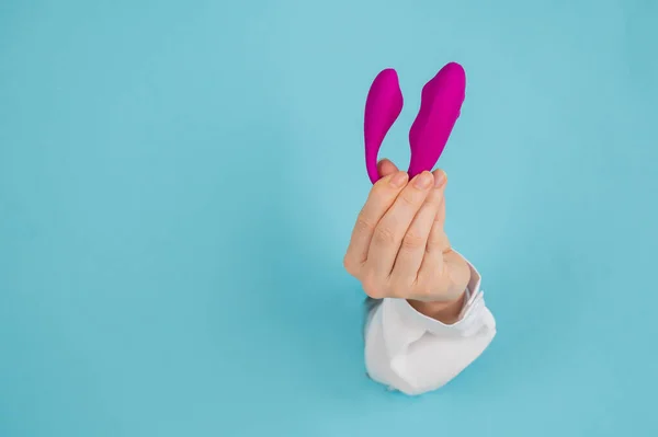 一只女人的手把一个粉色的性爱玩具从蓝色底色的纸孔里抱了出来. — 图库照片