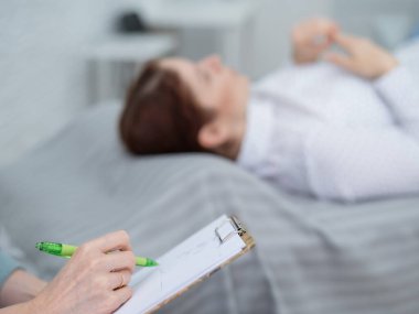Kafkasyalı bir kadın kanepeye uzanıp duygularını ifade ederken, bir psikolog tablete notlar alır.. 