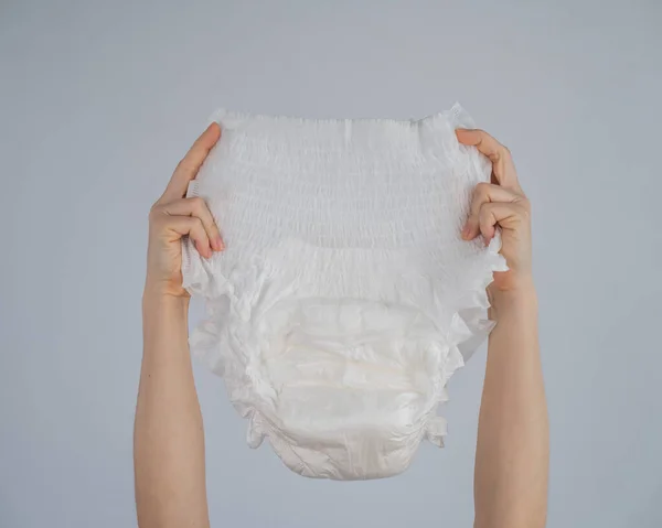 Una mujer sostiene un pañal adulto sobre un fondo blanco. Problemas de incontinencia. —  Fotos de Stock