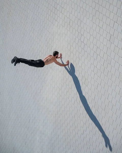 Tişörtsüz bir adam dışarıda elini kolunu sallayarak yürüyor. Yukarıdan görüntüle.