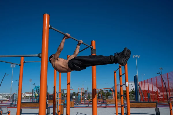 Açık havada üstsüz bir adam yatay barda beyaz giyiniyor.. 