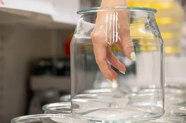 Mano femminile in un barattolo di vetro vuoto. Una fila di contenitori da cucina trasparenti in un negozio. — Foto Stock