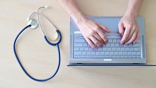 Вид сверху рук на клавиатуре. Женщина-врач за столом печатает на ноутбуке. Медсестра заполняет электронную карту пациента. — стоковое видео