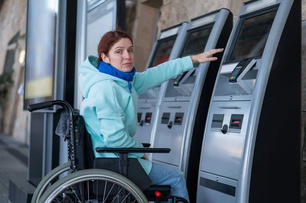 Een blanke vrouw in een rolstoel bereikt de zelfbedieningskassa op het station niet. Moeilijk bereikbare omgeving. — Stockfoto