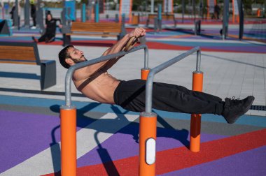 Spor sahasındaki paralel çubuklarda üstsüz adam yatay denge yapıyor.. 