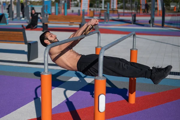 Póló nélküli férfi vízszintes egyensúlyt csinál párhuzamos rúdakon a sportpályán. — Stock Fotó