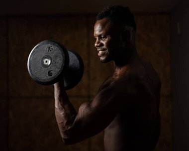 Çekici Afrikalı Amerikalı adam gülümsüyor ve halterlerle egzersiz yapıyor.. 
