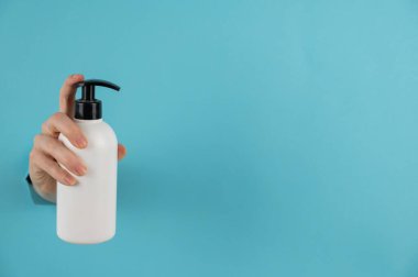 Bir kadın mavi bir kağıdın arka planında bir delikten dışarı çıkar ve bir cilt losyonu pompası tutar..