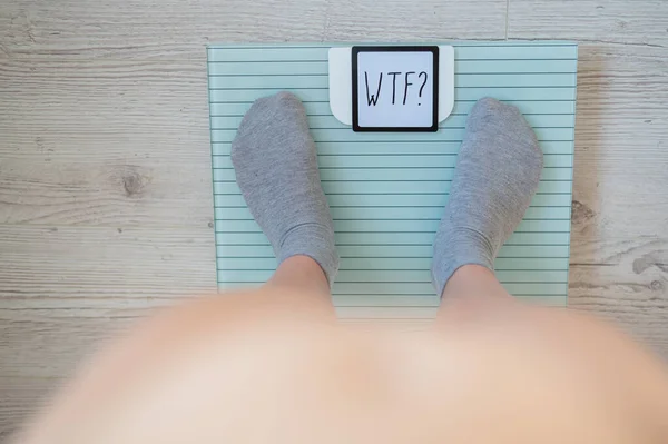 Top view on female legs in gray socks on electronic scales. Very heavy weight. The surprise of the increase in kg on a diet. The question is what the fuck.
