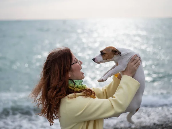 Biała rudowłosa kobieta trzymająca na wybrzeżu psa Jacka Russella Terriera. — Zdjęcie stockowe