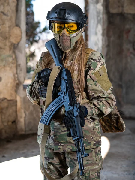Портрет женщины в шлеме и очки с автоматом в руках. Женщина-солдат в камуфляжной форме держит оружие.. — стоковое фото