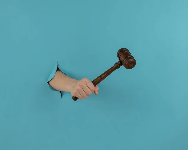 A womans hand with a wooden judges gavel sticks out of a hole in a blue background. — Stock Photo, Image