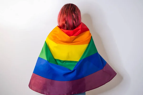 Joven mujer pelirroja está de pie con la espalda sobre un fondo blanco y sostiene la bandera lgbt —  Fotos de Stock