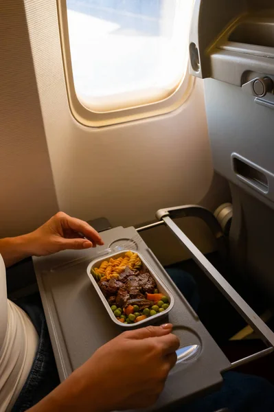 Caucasian woman flying in economy class and eating lunch from a tray table on board the plane. — Stock Photo, Image