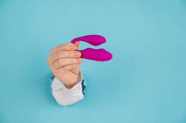 Bir kadının eli pembe bir seks oyuncağını kağıt mavisi bir arka planda bir delikten tutar.