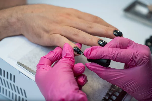 Een man op een manicure procedure schildert zijn nagels zwart in een schoonheidssalon — Stockfoto