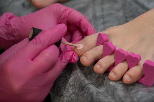 El maestro hace una pedicura aplica esmalte rosa en las uñas. — Foto de Stock